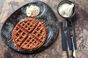 Nutella Waffle with chocolate, whipped cream, knife and fork served in dish isolated on dark background top view cafe dessert food photo