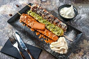 Assorted waffle sticks with Nutella, Oreo, Lotus, Brownie, Pistachio, Chocolate, Whipped cream, knife and fork served in dish isolated on dark background top view cafe dessert food photo