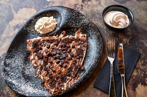 Oreo and Brownie Crepe with whipped cream, knife and fork served in dish isolated on dark background closeup top view of cafe baked dessert food photo