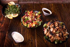 Assorted salads with tomato, cucumber, onion, cabbage, lettuce leaves, lemon slice, spinach and red beans served in dish isolated on wooden table side view of arabic food photo