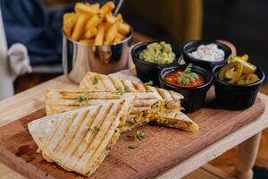 Chicken Quesadillas taco wrap slice with chili sauce and french fries bucket served on wooden board isolated on table top view of arabic fastfood photo