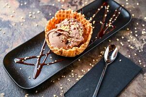 ferrero rocher helado con hielo crema, blanco chocolate chip, y cuchara servido en cono aislado en oscuro antecedentes de cerca parte superior ver de café horneado postre comida foto