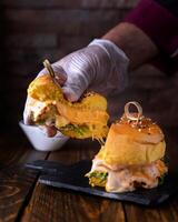 Stuffed Chicken Burger Holding in Hand with melted cheese, chicken, lettuce leaves and egg served in dish isolated on wooden table side view of arabic food photo