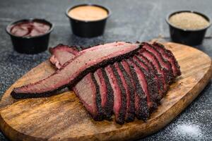 Beef Brisket platter steak meat sliced isolated on wooden board with dip sauce top view of grill food on dark grey background photo