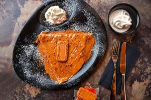 Lotus Crepe cookie with whipped cream, knife and fork served in dish isolated on dark background closeup top view of cafe baked dessert food photo