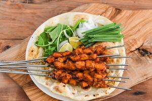 Swek of Chicken Tikka with bahraini bread tandoori nan, lime and salad served in dish isolated on wooden table top view middle eastern grills food photo