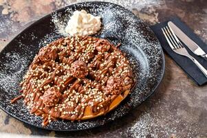 ferrero rocher gofre con chocolate, azotado crema, cuchillo y tenedor servido en plato aislado en oscuro antecedentes parte superior ver café postre comida foto