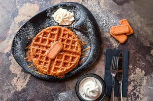 Lotus Waffle with chocolate, whipped cream, knife and fork served in dish isolated on dark background top view cafe dessert food photo