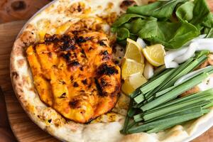 Tandoori Boneless chicken with bahraini bread tandoori nan, lime and salad served in dish isolated on wooden table top view middle eastern grills food photo