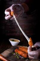 Deep Fried Mozzarella Sticks in hand served in cutting board isolated on wooden table side view of arabic food photo