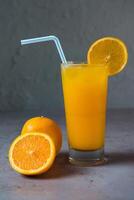 sano recién exprimido naranjas Fresco jugo servido en vaso con naranja rebanada y Paja lado ver en gris antecedentes foto