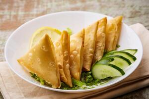 Deep Fried Sambosa Cheese samosa triangle wrap with lime and cucumber served in dish isolated on table top view of arabic food photo