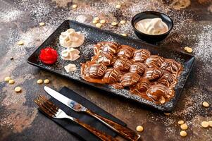 Marble Poffers with chocolate, whipped cream, knife and fork served in dish isolated on dark background closeup top view of cafe baked dessert food photo