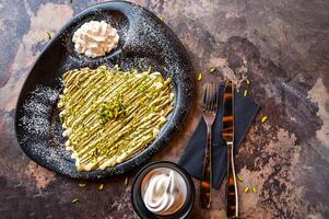 Pistachio Crepe With White chocolate with whipped cream, knife and fork served in dish isolated on dark background closeup top view of cafe baked dessert food photo