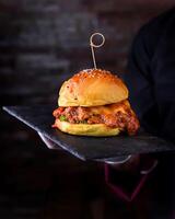 Buffalo Chicken Burger with sauce and lettuce leaves served in cutting board holding in hand isolated on wooden table side view of arabic food photo