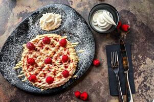 Raspberry Waffle with white chocolate, whipped cream, knife and fork served in dish isolated on dark background top view cafe dessert food photo