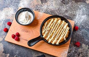 White Chocolate and Raspberry Cookie Dough with white chocolate, whipped cream, knife and fork served in dish isolated on dark background closeup top view of cafe baked dessert food photo