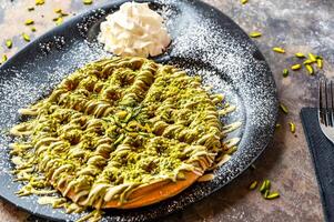 Pistachio Waffle with chocolate, whipped cream, knife and fork served in dish isolated on dark background top view cafe dessert food photo