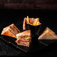 Club sandwiches with french fries bucket served in dish isolated on wooden table side view of arabic food photo