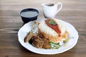 Fattah with meat or boiled rice with beef and sauce served in dish isolated on wooden table side view of arabic food photo