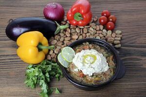 Foul baba ghanoush with cherry tomato, bell pepper, onion, lime and coriander served in dish isolated on wooden table side view of arabic food photo