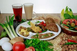 Arabic Dynamite breakfast platter with flafel, marinated fried eggplant, mashed potato, hummus, foul, beans, pita bread, salad and coffee drink isolated on table side view photo