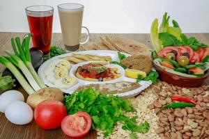 Egyptian Dynamite breakfast platter with flafel, marinated fried eggplant, boiled egg, hummus, potato, foul, beans, pita bread, salad and coffee drink isolated on table side view photo