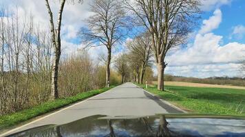View from the windshield of a moving car onto a small and narrow country road with trees and bushes on the side. video