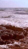 Forte ondas e salpicos falhando e espirrando em a pedras em uma ensolarado dia e rude mar. poderoso mar ondas quebra sobre pedras em de praia mega limnionas, quios, Grécia video