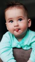 A baby with a green shirt is looking at the camera video