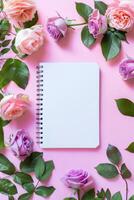 Notebook Surrounded by Flowers on Pink Background photo