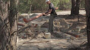 un' lavoratore, rivestito nel opera abbigliamento e attrezzata con sicurezza Ingranaggio, è nel il processi di posa grande metropolitana tubi tra il parzialmente sepolto calcestruzzo fondamenta nel un' foreste costruzione luogo. video