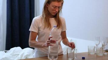 Woman in pajamas and glasses drink a glass of water in the morning standing by the bed video