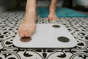 Woman checking her weight on weighing scales in bathroom photo