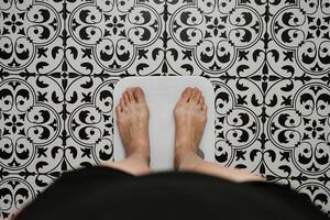 Woman checking her weight on weighing scales in bathroom photo