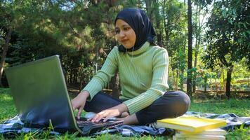 Asian girl muslim student using laptop at park, resting and studying outdoors, free space photo