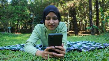contento musulmán mujer teniendo vídeo llamada en móvil teléfono a parque, utilizando auriculares, gratis espacio foto