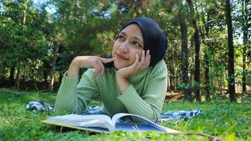 Smiling muslim woman in hijab in park holding book and pen thinking idea.Empty space photo