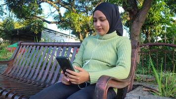 Happy muslim woman listen music on mobile phone at park, using headset, free space photo