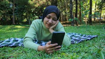 Happy muslim woman having video call on mobile phone at park, using headset, free space photo