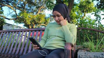 Happy muslim woman listen music on mobile phone at park, using headset, free space photo