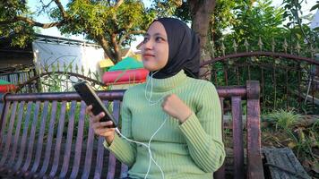 contento musulmán mujer escucha música en móvil teléfono a parque, utilizando auriculares, gratis espacio foto