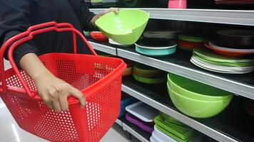 a woman shopping for plastic bowls and plates in a supermarket holding a basket. photo