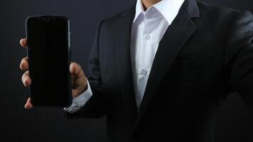 Businessman in a black suit showing smartphone with vertical blank white screen.Horizontal mockup photo