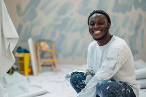 ai generado sonriente joven hombre agachado abajo pintura un pared con un gris pintar rodillo en un brillante habitación con mueble cubierto en hojas foto