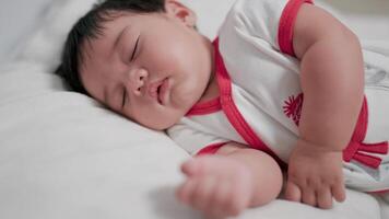 Close-up face of chubby newborn baby lying on stomach, eyes open and smiling with blanket on bed. video