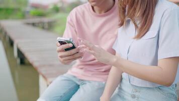 fermer photo de une couple Planification leur Voyage des plans sur une téléphone intelligent en ligne, séance sur une pont par une rivière étang, le plus romantique Matin atmosphère. le idée de exprimer l'amour. video