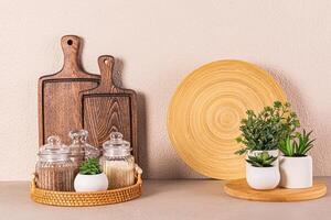 Set of glass jars with spices on a round wicker tray on a stone countertop. Potted houseplants. Kitchen background. Front view. photo