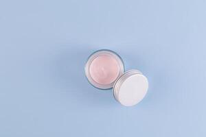 Open Glass Transparent Jar With Pink Cream For Young Skin Face And Body On Blue Background With Copy Space. Natural cosmetics. photo