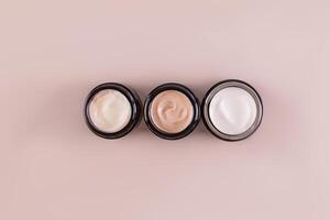 A jars with cosmetic cream of different textures and colors for face and body skin care. Beige background. space for text. Top view. photo